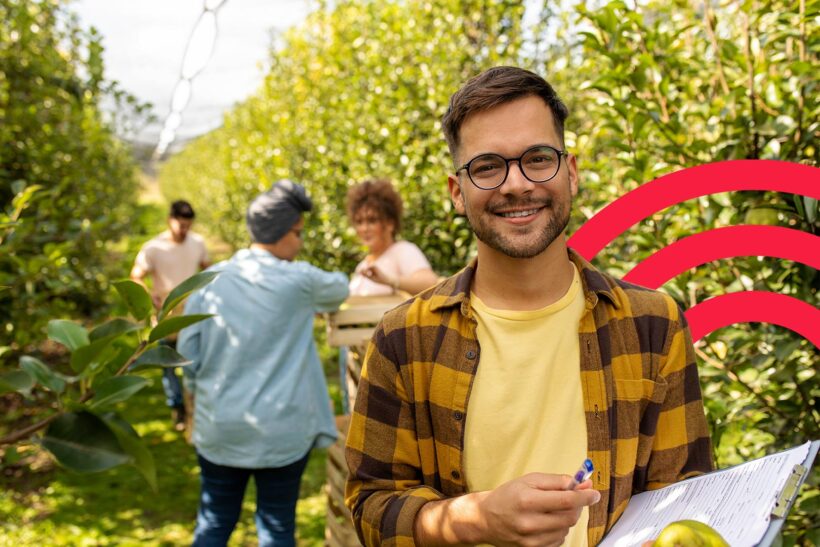 Young man in orchard smiling with people working in the background